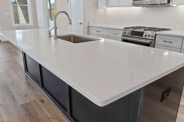 kitchen featuring high end stove, a kitchen island with sink, and white cabinets