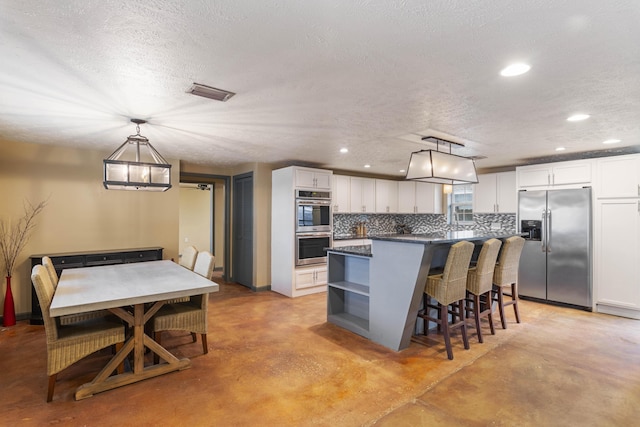 kitchen with stainless steel appliances, tasteful backsplash, visible vents, white cabinets, and concrete flooring