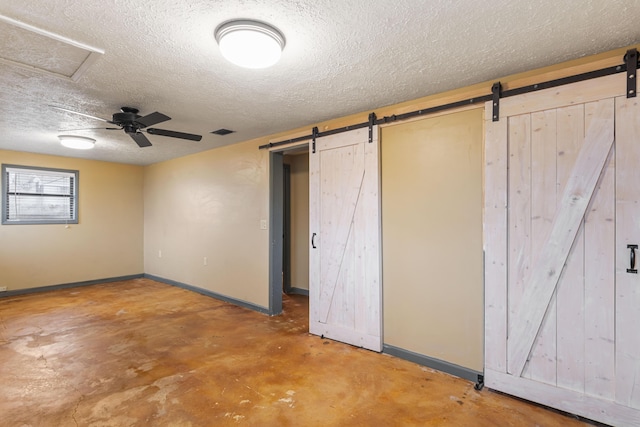 below grade area featuring a barn door, baseboards, visible vents, a ceiling fan, and a textured ceiling