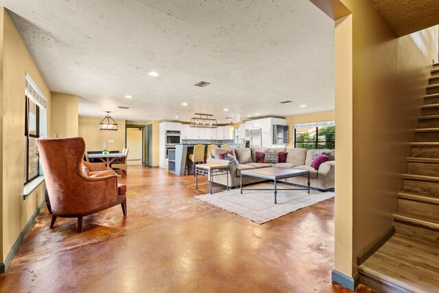 living room featuring finished concrete flooring, stairs, visible vents, and a textured ceiling