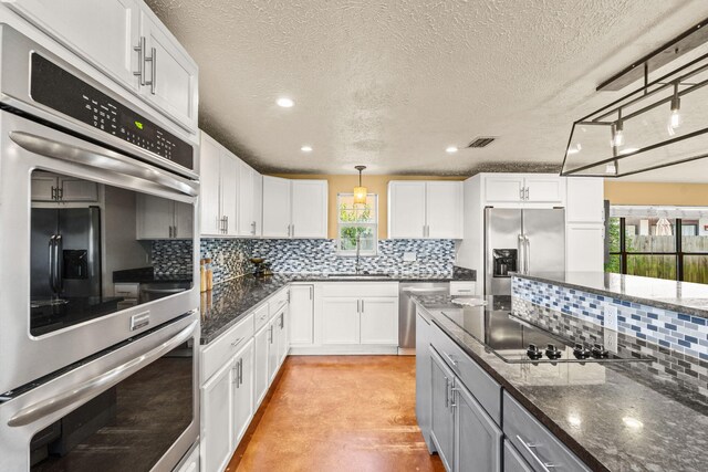 kitchen featuring visible vents, white cabinets, hanging light fixtures, appliances with stainless steel finishes, and backsplash