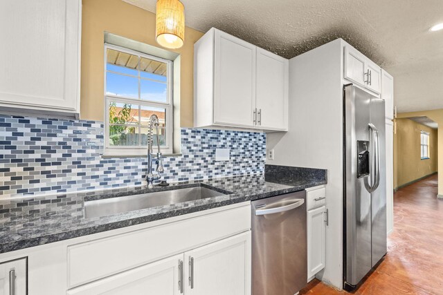 kitchen with stainless steel appliances, backsplash, white cabinetry, a sink, and dark stone countertops