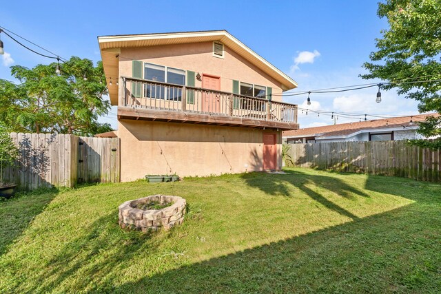 rear view of property featuring a fenced backyard, a lawn, a fire pit, and stucco siding