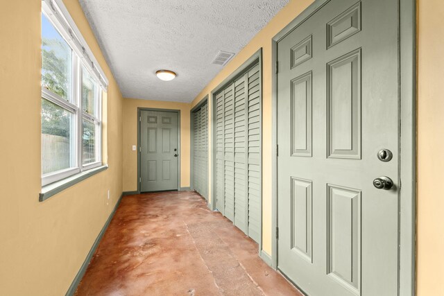 hall with baseboards, a textured ceiling, visible vents, and concrete flooring