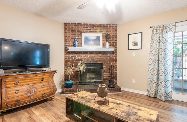 living room featuring a textured ceiling, a fireplace, a ceiling fan, baseboards, and light wood finished floors