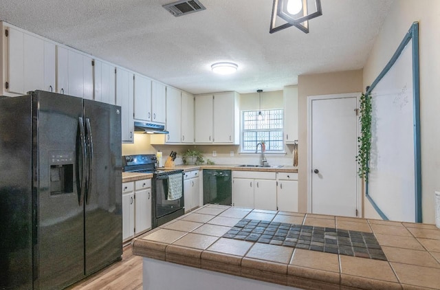 kitchen featuring tile counters, white cabinets, under cabinet range hood, black appliances, and a sink