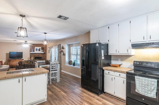 kitchen with white cabinets, open floor plan, under cabinet range hood, black appliances, and pendant lighting