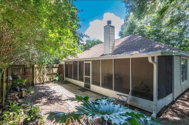 back of property with a sunroom, a chimney, roof with shingles, fence, and a patio area