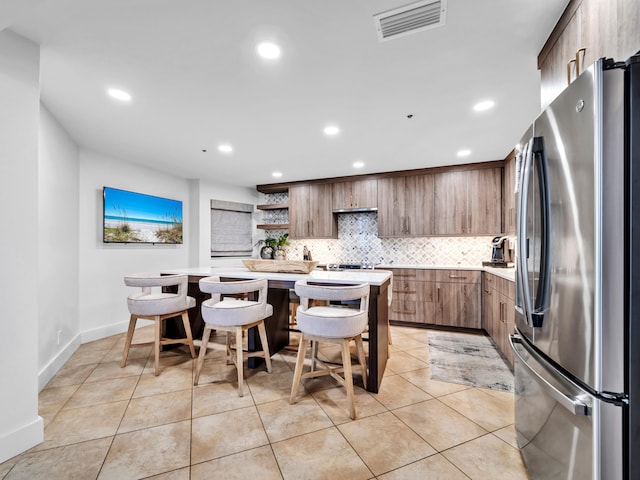 kitchen featuring a kitchen island, stainless steel refrigerator, backsplash, a kitchen bar, and light tile patterned floors