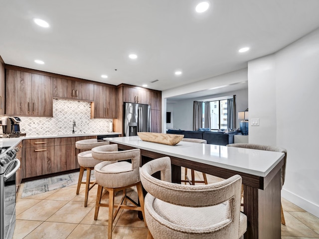 kitchen featuring sink, a breakfast bar area, light tile patterned floors, appliances with stainless steel finishes, and decorative backsplash