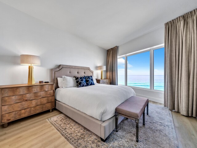 bedroom with a water view, lofted ceiling, and light hardwood / wood-style flooring