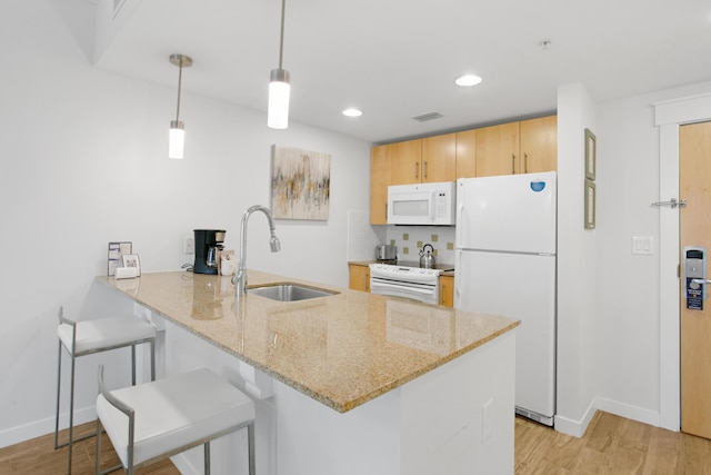 kitchen with kitchen peninsula, light stone countertops, white appliances, sink, and pendant lighting