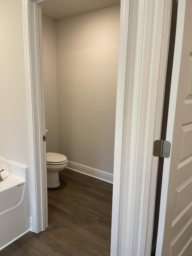 bathroom with wood-type flooring, a tub to relax in, and toilet