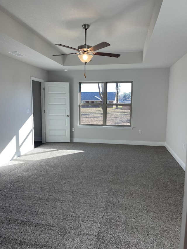 unfurnished room featuring dark colored carpet, a tray ceiling, and ceiling fan