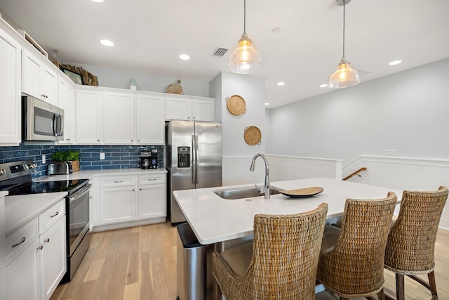 kitchen with visible vents, light wood-style flooring, a sink, stainless steel appliances, and backsplash