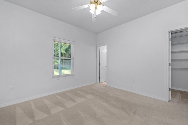 unfurnished bedroom with light carpet, a walk in closet, a closet, and ceiling fan