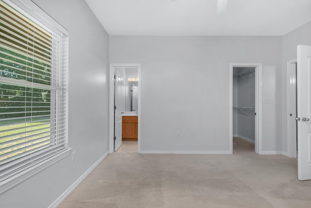 unfurnished bedroom with light carpet, a walk in closet, a closet, and ensuite bathroom