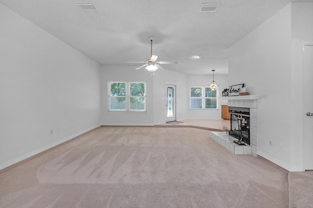 unfurnished living room with a tiled fireplace, ceiling fan, light carpet, and a textured ceiling