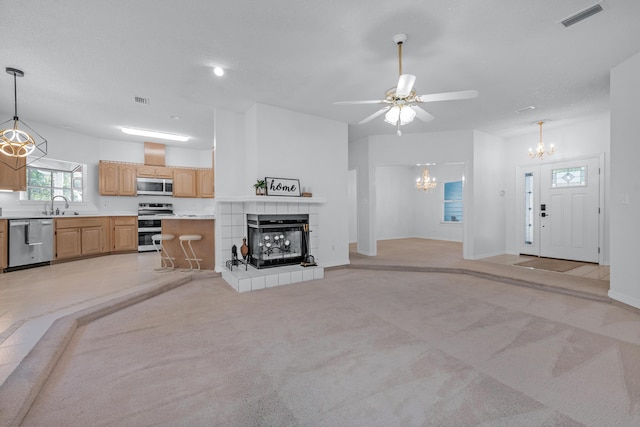 unfurnished living room featuring a tiled fireplace, sink, ceiling fan with notable chandelier, and light colored carpet