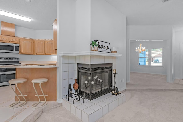 kitchen featuring appliances with stainless steel finishes, light brown cabinetry, a kitchen bar, a tiled fireplace, and light colored carpet