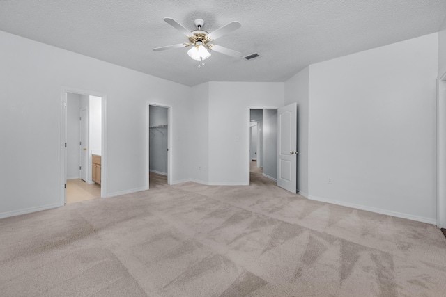 unfurnished bedroom featuring ensuite bath, a walk in closet, ceiling fan, a textured ceiling, and a closet