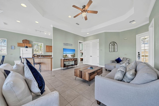 living room featuring track lighting, crown molding, ceiling fan, a tray ceiling, and light tile patterned flooring