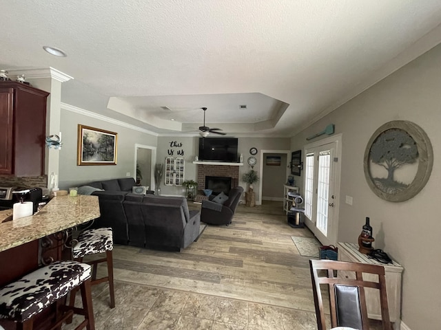 living room with a textured ceiling, ornamental molding, a tray ceiling, ceiling fan, and a fireplace