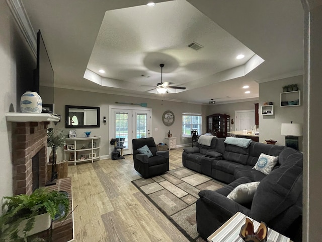 living room with ornamental molding, a tray ceiling, a brick fireplace, and light wood-type flooring