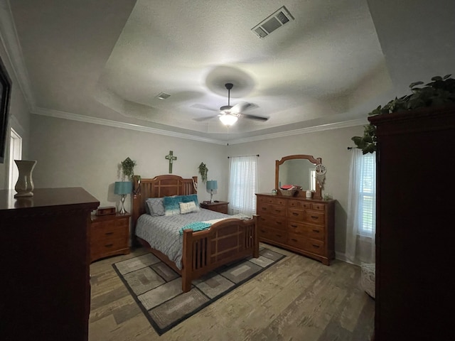 bedroom featuring crown molding, ceiling fan, light hardwood / wood-style floors, a textured ceiling, and a raised ceiling