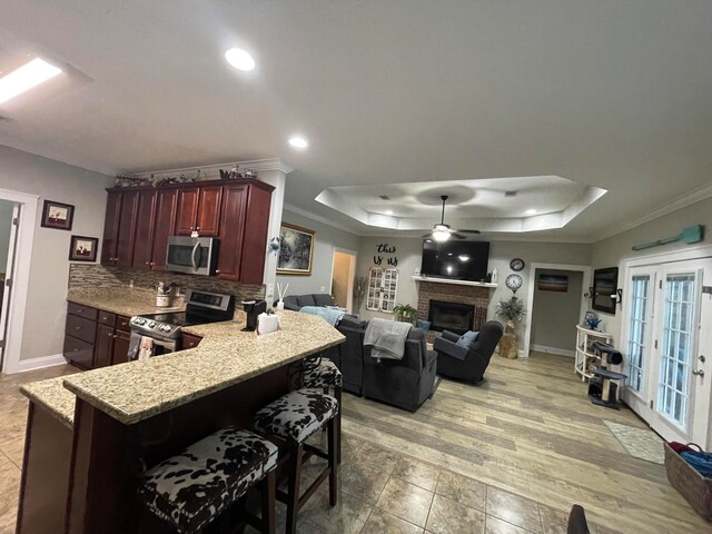 kitchen with crown molding, stainless steel appliances, a tray ceiling, a kitchen bar, and a brick fireplace