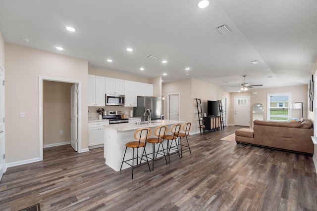 kitchen with white cabinetry, ceiling fan, stainless steel appliances, an island with sink, and dark wood-type flooring