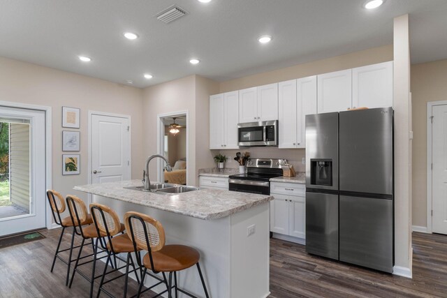 kitchen with dark wood-type flooring, appliances with stainless steel finishes, white cabinets, and a kitchen island with sink