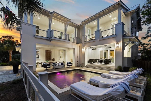 back house at dusk with a fenced in pool, ceiling fan, a balcony, and an outdoor hangout area