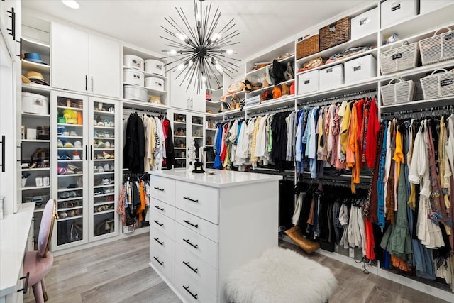 spacious closet with an inviting chandelier and light hardwood / wood-style flooring