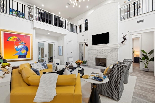 living room featuring light wood-type flooring, a towering ceiling, french doors, and a brick fireplace