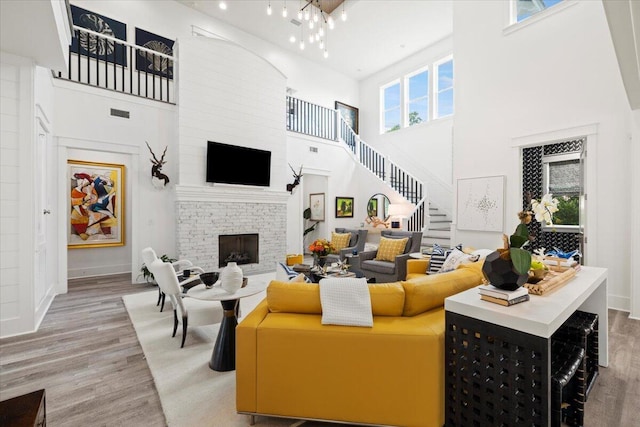 living room featuring a fireplace, a high ceiling, light hardwood / wood-style flooring, and a notable chandelier