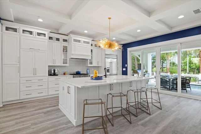 kitchen with decorative backsplash, light wood-type flooring, a center island with sink, and white cabinetry