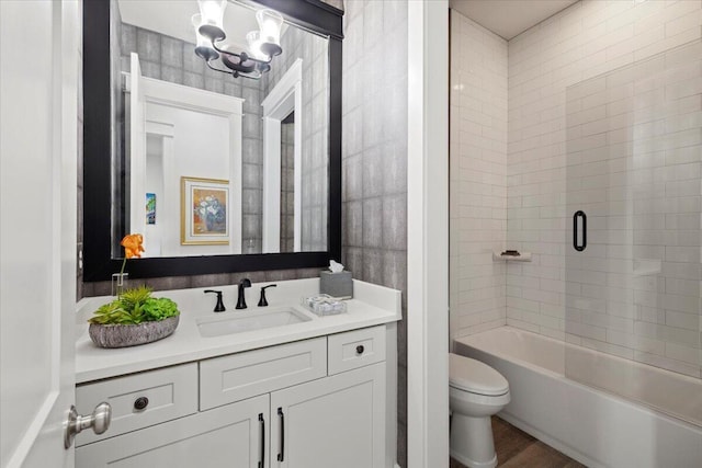 full bathroom with tiled shower / bath combo, an inviting chandelier, wood-type flooring, toilet, and vanity