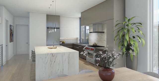 kitchen featuring sink, high end range, a center island with sink, light wood-type flooring, and wall chimney exhaust hood