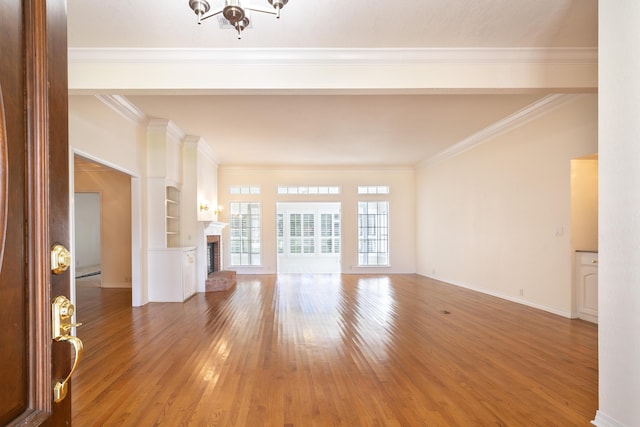 unfurnished living room with built in shelves, ornamental molding, a fireplace, and hardwood / wood-style floors