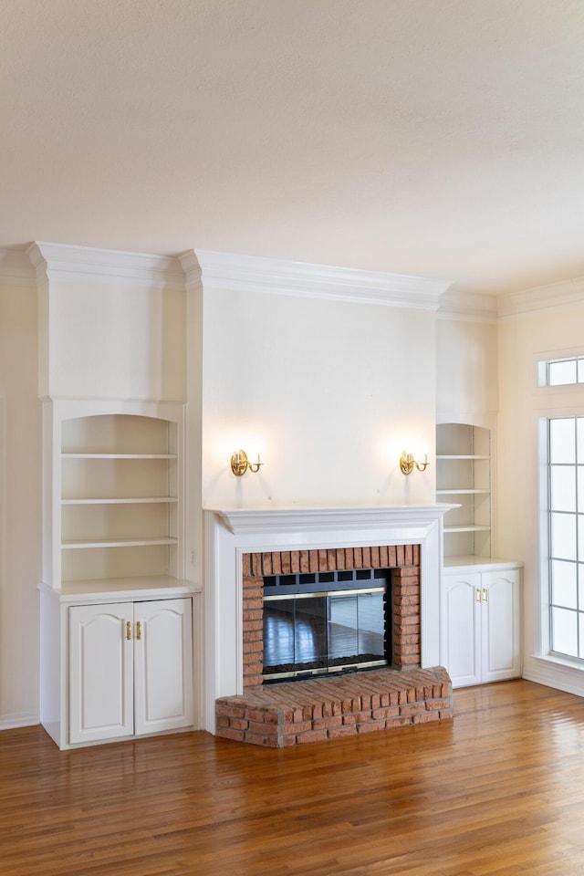 unfurnished living room with crown molding, built in shelves, a fireplace, and wood-type flooring