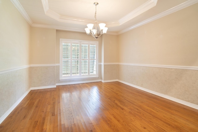 empty room featuring crown molding, wood-type flooring, a raised ceiling, and a chandelier