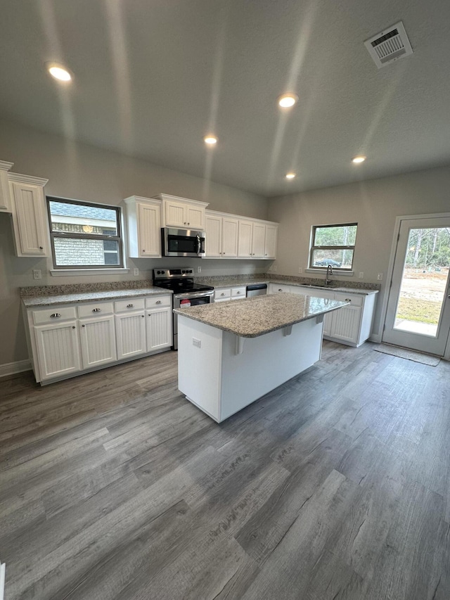 kitchen with white cabinets, a center island, light wood-type flooring, and appliances with stainless steel finishes