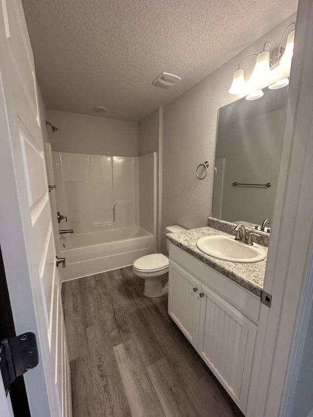 full bathroom with hardwood / wood-style floors, shower / bath combination, a textured ceiling, toilet, and vanity