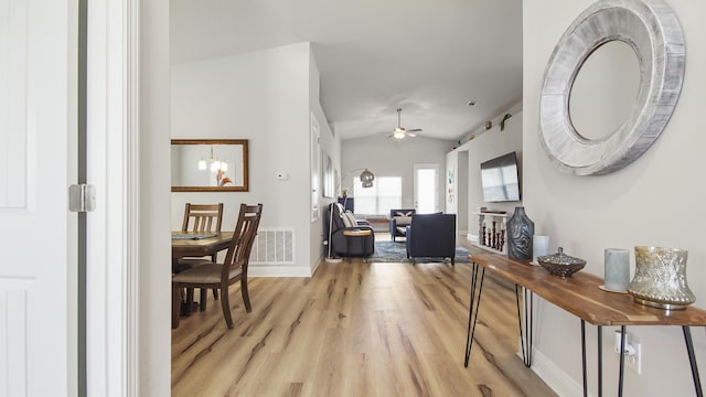 hallway with a notable chandelier, lofted ceiling, visible vents, light wood-type flooring, and baseboards