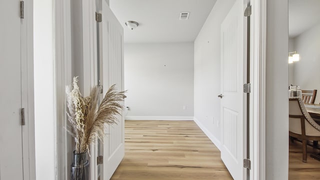 hall with light wood-style flooring, visible vents, and baseboards