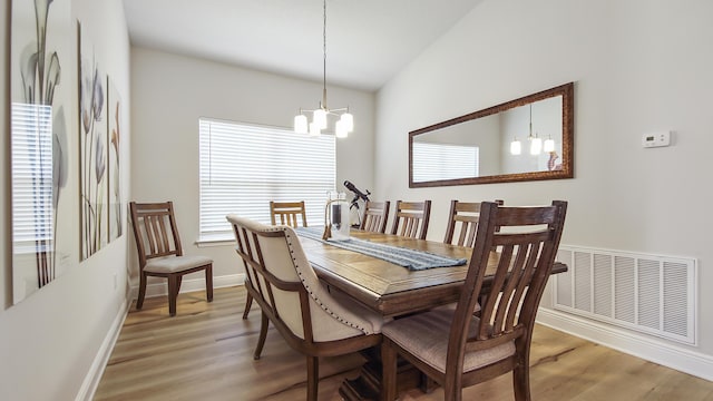 dining area with an inviting chandelier, visible vents, vaulted ceiling, and wood finished floors