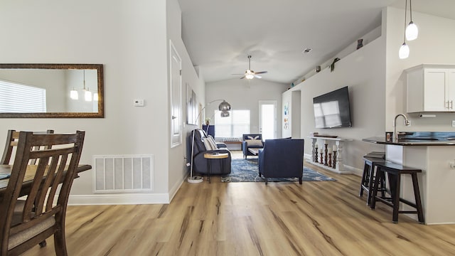 living area featuring visible vents, baseboards, lofted ceiling, ceiling fan, and light wood-type flooring