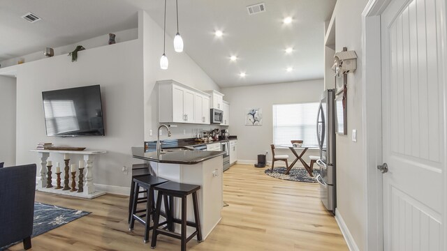 kitchen featuring lofted ceiling, light wood-type flooring, white cabinets, stainless steel appliances, and decorative light fixtures