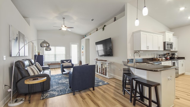 living area featuring vaulted ceiling, light wood finished floors, a ceiling fan, and baseboards